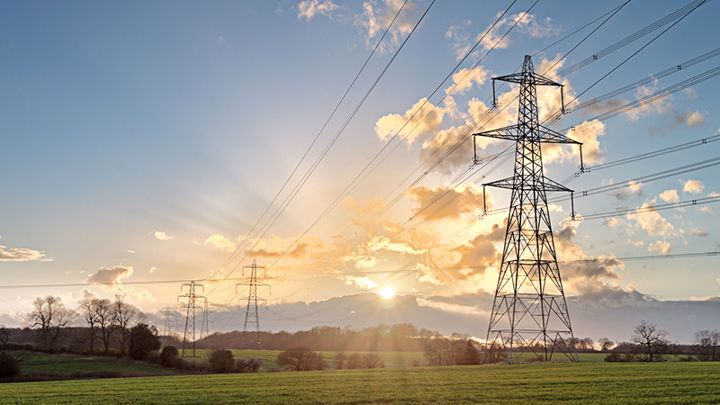 Electricity pylons and power lines across a grassy field at sunset